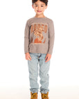Full body view of boy wearing Chaser’s Hold Your Horses dark grey long sleeve with cowboy graphic, jeans, and boots on a white background