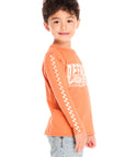 Side view of boy wearing Chaser’s Raceway Speed orange long-sleeve top with racing checker detail in white on the sleeve on a white background