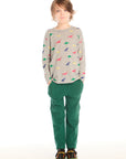Full body view of boy wearing Chaser’s Multi Dinos grey long sleeve top with colorful dinosaur patterns and green pants on a white background