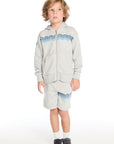 Full body view of boy wearing the Chaser Kids Peace Out Shorts in Heather Grey styled with the matching Peace Out Zip-Up Hoodie featuring blue wave graphics across the chest and shorts, paired with white socks and navy sneakers on a white background