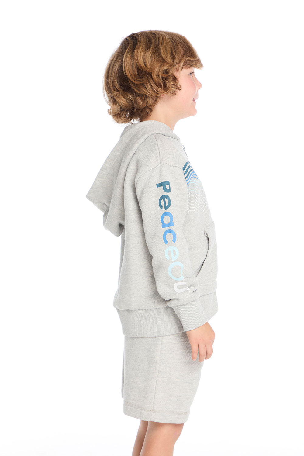 Side view of boy wearing Chaser Kids Peace Out Zip Up Hoodie in Heather Grey showing “Peace Out” text on sleeve, white background