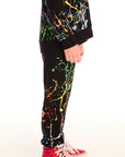 Side view of boy wearing Chaser’s Paint Splatter black pants with colorful splatter design against a white background