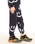 Side view of boy wearing Chaser's navy Allover Smileys Pants with white patterns on a white background