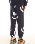 Back view of boy wearing Chaser's navy Allover Smileys Pants with white patterns on a white background