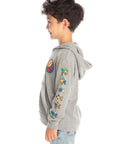 Side view of boy wearing Chaser’s The Grateful Dead Colorblocked Stealie heather grey zip up hoodie featuring colorful Dancing Bears on the sleeve, paired with light blue jeans and brown boots on a white background
