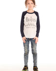 Full body view of boy wearing Chaser’s The Beatles Abbey Road football tee in white with navy blue sleeves and jeans on a white background