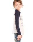 Side view of boy wearing Chaser’s The Beatles Abbey Road football tee in white with navy blue sleeves and jeans on a white background