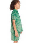 Side view of boy wearing the Chaser Kids Wild Green Tie Dye Polo Shirt showing short sleeves and relaxed fit, styled with matching tie dye shorts and silver sneakers on a white background