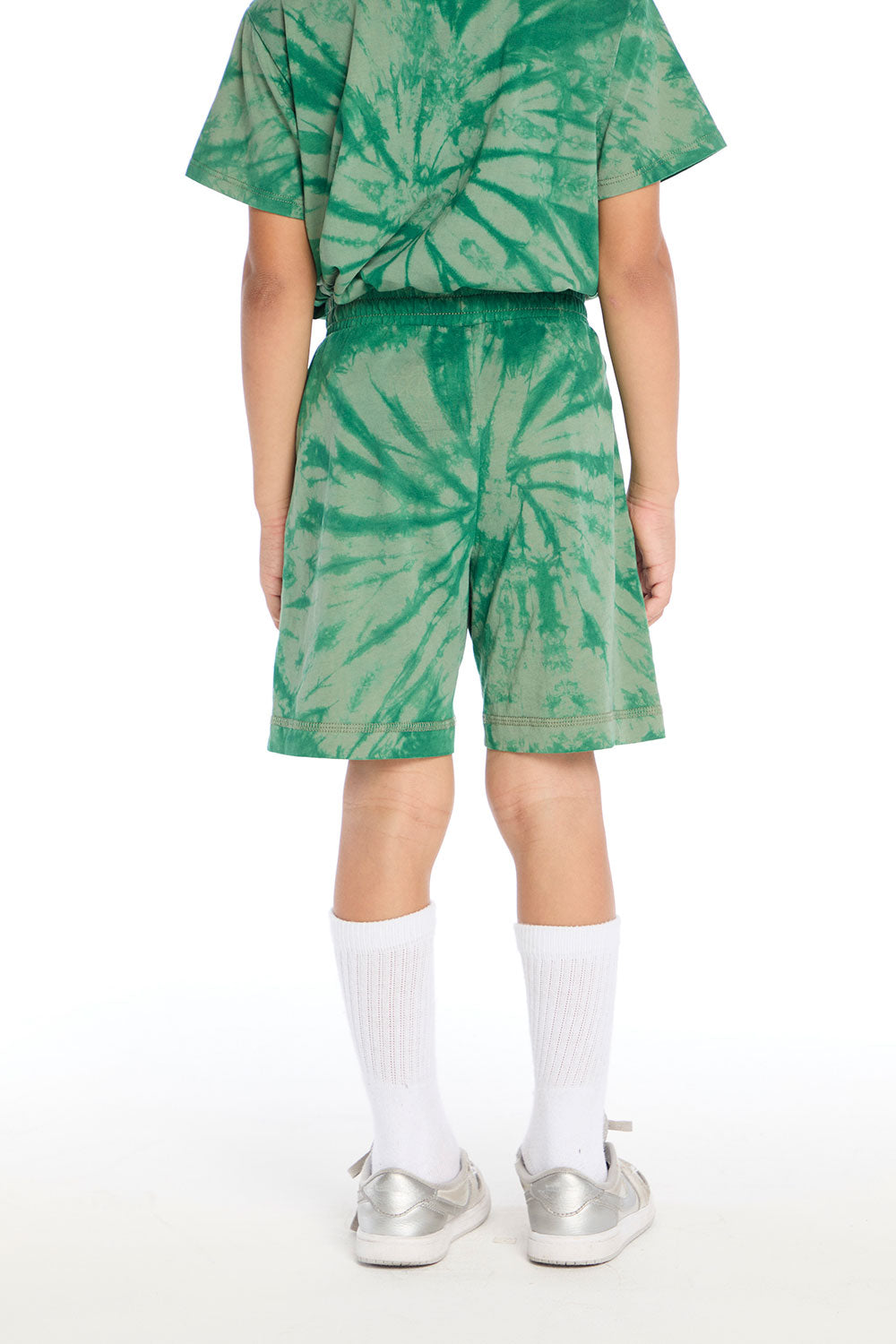 Back view of boy wearing the Chaser Kids Wild Green Tie Dye Cozy Beach Shorts featuring the same spiral tie dye pattern across the shorts, styled with matching top on a white background