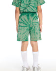 Back view of boy wearing the Chaser Kids Wild Green Tie Dye Cozy Beach Shorts featuring the same spiral tie dye pattern across the shorts, styled with matching top on a white background