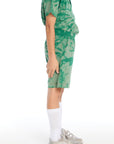 Side view of boy wearing the Chaser Kids Wild Green Tie Dye Cozy Beach Shorts showing pockets and relaxed fit, paired with matching tie dye polo on a white background