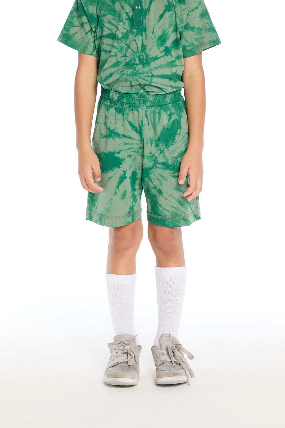 Front view of boy wearing the Chaser Kids Wild Green Tie Dye Cozy Beach Shorts with an elastic waistband and spiral tie dye pattern, paired with the matching Wild Green Tie Dye Polo Shirt on a white background
