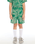 Front view of boy wearing the Chaser Kids Wild Green Tie Dye Cozy Beach Shorts with an elastic waistband and spiral tie dye pattern, paired with the matching Wild Green Tie Dye Polo Shirt on a white background