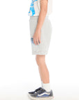 Side view of boy wearing the Chaser Kids Peace Out Shorts in Heather Grey showing side pockets and blue wave design, styled with a graphic tee and navy sneakers on a white background