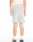 Back view of boy wearing the Chaser Kids Peace Out Shorts in Heather Grey paired with a white tee and navy sneakers on a white background