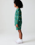 Side view of boy wearing Chaser's green Dino Party Shorts and matching Pullover against a white background