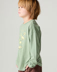 Side view of a boy wearing the Chaser Dino Action Boys Tee on a neutral background with hands in pockets of brown pants
