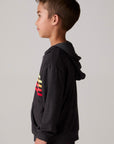 Model wearing Chaser's Vintage Black Stripe Boys Zip-Up Hoodie in Black with striped detailing, side view
