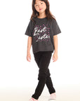 Full body view of young girl wearing Chaser’s Best Sister black tee with black jeans on a white background