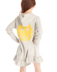 Back view of girl wearing Chaser’s Glitter Smiley Heather Grey Hoodie Dress with long sleeves and a large yellow smiley face graphic on the back against a white background