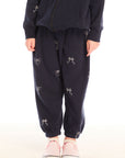 Girl wearing Chaser’s navy blue Tossed Glitter Bows Pants with embroidered bow designs on a white background