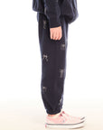 Side view of girl wearing Chaser’s navy blue Tossed Glitter Bows Pants with embroidered bows on a white background