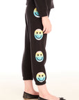 Side view of girl wearing Chaser’s black Pastel Rainbow Smiley Pants with pastel-colored smiley face designs on a white background