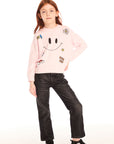 Full body view of young girl wearing Chaser’s pink Be Happy Icons long sleeve pullover with smiley face design and black jeans on a white background