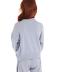 Back view of girl wearing Chaser’s blue-gray Pastel Love Bolt Long Sleeve with colorful “LOVE” design on a white background