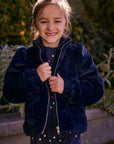 Chaser Kids Avalon Girls Puff-Sleeve Jacket in navy plush fabric with a front zipper, front view outdoors beside a low wall and greenery