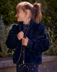 Chaser Kids Avalon Girls Puff-Sleeve Jacket in navy plush fabric, front three-quarter view outdoors beside a low wall and greenery