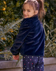 Chaser Kids Avalon Girls Puff-Sleeve Jacket in navy plush fabric, rear three-quarter view outdoors beside a low wall and greenery