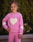 Chaser Kids Holiday Hug Girls Hoodie in pink with white hearts, front view outdoors beside a low wall and greenery