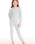 Full body view of girl wearing Chaser’s Slim Snowflake Legging pants with matching Cropped Shirred Snowflake Pullover Hoodie in light blue with pink heart sleeve accents on a white background