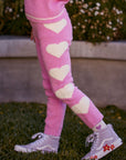 Chaser Kids Holiday Hug Girls Pants in pink, side detail of white hearts outdoors beside a low wall and greenery