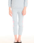 Girl wearing Chaser’s Slim Snowflake Legging pants with pink hearts on legs and matching Cropped Shirred Snowflake Pullover Hoodie in light blue with pink heart sleeve accents on a white background