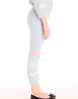 Side view of girl wearing Chaser’s Slim Snowflake Legging pants with pink hearts on legs and matching Cropped Shirred Snowflake Pullover Hoodie in light blue with pink heart sleeve accents on a white background