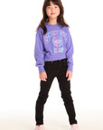 Full body view of girl wearing Chaser’s purple Snow Day Athletic Club long sleeve with text and graphics and black jeans on a white background