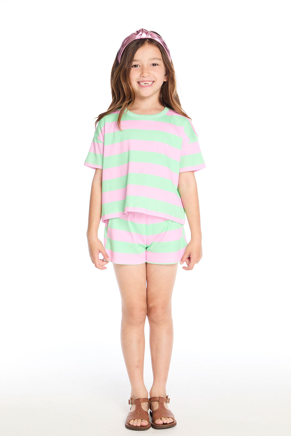 Girl wearing the Chaser Kids Pinky Aloe Stripe Jade Short paired with the matching Pinky Aloe Stripe Devin Tee, styled with sandals and a metallic pink headband on a white background