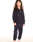 Full body view of girl wearing Chaser’s navy blue Tossed Glitter Bows Pants with embroidered bows and matching zip up hoodie on a white background