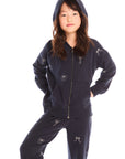 Girl wearing Chaser’s navy blue Tossed Glitter Bows Zip Up Hoodie with hood up and matching pants with embroidered bow designs on a white background