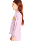 Side view of girl wearing Chaser’s pink Rainbow Glitter Heart Pullover with rainbow heart design on a white background