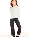 Full body view of young girl wearing Chaser’s Ciao Allover Stars light green pullover with light grey star patterns and dark jeans on a white background