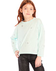 Young girl wearing Chaser’s Ciao Allover Stars light green pullover with light grey star patterns and dark jeans on a white background