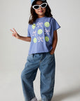 Full body front view of a girl wearing the Chaser Happy Bows Tee with sunglasses and a hat on a neutral background