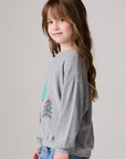 Model wearing Chaser's Festive Trees Girls Pullover in heather grey with distinctive graphic and design details, side view