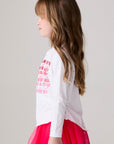 Model wearing Chaser's Merry Girls Long Sleeve Tee in white with pink and red Merry lettering, side view
