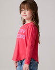 Model wearing Chaser's Howdy Holidays Girls Long Sleeve Tee in hibiscus with western holiday graphic, side view