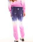 Back view of girl wearing Chaser’s Slim Ombre Tie Dye Pants with colorful glitter star patterns and matching long sleeve top on a white background