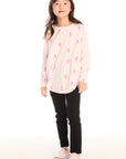 Young girl wearing Chaser's light pink Allover Pink Skiers Long Sleeve top with pink patterns and black pants on a white background